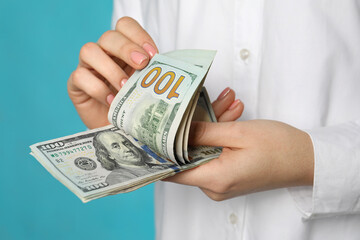 Woman counting dollar banknotes on turquoise background, closeup. Money exchange concept