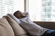 © fizkes - Happy relaxed young African man resting on sofa in home apartment, leaning on back, breathing fresh air, looking at big window, city buildings view, enjoying break, leisure, thinking, dreaming