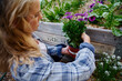 © StratfordProductions - Profile view of young caucasian woman in checked shirt holding flowers in plant nursery