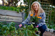 © StratfordProductions - Happy young caucasian woman looking at camera while crouching by flowerbed in plant nursery
