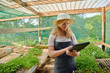 © StratfordProductions - Young caucasian woman wearing apron using digital tablet by plants in plant nursery
