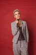 Attractive happy glamorous blonde short haired host singer blogger woman in checked suit and white hills holding microphone in hand on red wall background