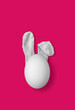 Bunny rabbit ears made of white fluffy socks with white egg on bright pink background. Easter minimal concept. Flat lay