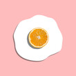 Orange slice instead of egg yolk forming fried egg on pastel pink background. Summer sunny side up egg minimal concept