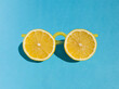 Yellow sunglasses made from fresh lemon slices and plastic lemonade straws on bright blue background. Summer minimal concept with sharp shadows. Funny idea