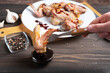 The hand holds the fork with the chicken wing and dips it in the teriyaki sauce. Dish of Asian cuisine