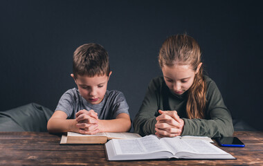 Wall Mural - Children pray with folded hands. The Bible is open on the table. Prayer to pray