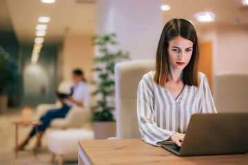 Adult businesswoman using a laptop, working with a female colleague at the office.