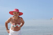 © alex.pin - signora anziana con il cappello colore fucsia si gode il sole  in riva al mare in costume da bagno