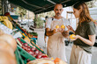 © Maskot - Male vendor wearing apron while assisting female customer buying lemons at market