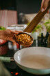 © Maskot - Hands of female chef adding chickpea in cooking pan using wooden spoon at studio kitchen