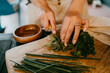© Maskot - Hands of female chef chopping leafy vegetable on cutting board in studio