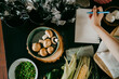 © Maskot - Hand of female chef writing recipe in diary by vegetables and cutlery on counter
