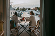© Maskot - Rear view of couple having tea while sitting on chair at porch by marina