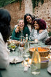 © Maskot - Happy female friends enjoying together at dining table during dinner party in back yard