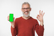 © InsideCreativeHouse - Smiling happy caucasian mature middle-aged man holding cellphone smart phone with mockup screen showing okay gesture isolated in white background