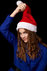 Poster - caucasian girl with long hair in a blue dress holds a hand in a santa claus hat isolated on a black background