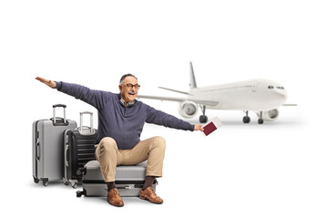 Poster - Mature man sitting on a suitcase with a passport and a ticket and spreading arms to fly