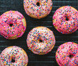© Cavan Images - Close up of vanilla cake donuts with pink icing and sprinkles.