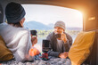 © Soloviova Liudmyla - Car trunk view of chatting couple dressed warm knitted clothes enjoying gas stove prepared coffee and mountain lake view. Cozy early autumn couple auto traveling concept image.