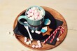 Chocolate with marshmallows in blue mug among winter decorations on wooden tray.