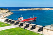 The guns on the Saluting Battery in Valletta, Malta, overlooking a tanker moored in Grand Harbour. Across the harbour is Fort Ricasoli and the Ricasoli Breakwater Lighthouse.