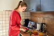 © Elena Medoks - A young woman prepares dinner or lunch from video recipes. Culinary blogs. Online cooking