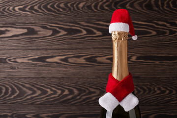 Wall Mural - Champagne bottle wearing christmas hat and red knitting scarf on wooden background. New Year concept