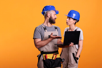 Team of constructors holding laptop and browsing internet online, discussing about renovation project. Construction workers using wireless pc to search building inspiration, studio shot.