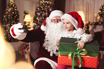 Canvas Print - Santa Claus and little girl taking selfie in room decorated for Christmas