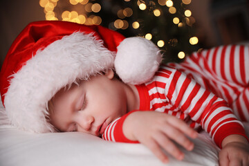 Canvas Print - Baby in Christmas pajamas and Santa hat sleeping on bed indoors