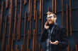 © YURII MASLAK - A young red-haired guy, in glasses, against the backdrop of a business center, in a stylish coat. Speaks confidently on the phone, solving problems on the go. Portrait of a successful young man.