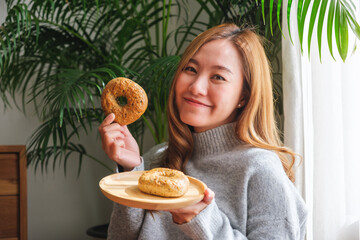 Portrait image of a young woman in sweater holding a plate of bagel at home