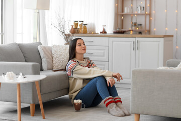 Wall Mural - Young woman in warm sweater sitting in kitchen