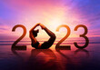 Happy new year card 2023. Silhouette of healthy girl doing Yoga One Legged Pigeon pose on tropical beach with sunset sky background, woman practicing yoga as a part of the Number 2023 sign.