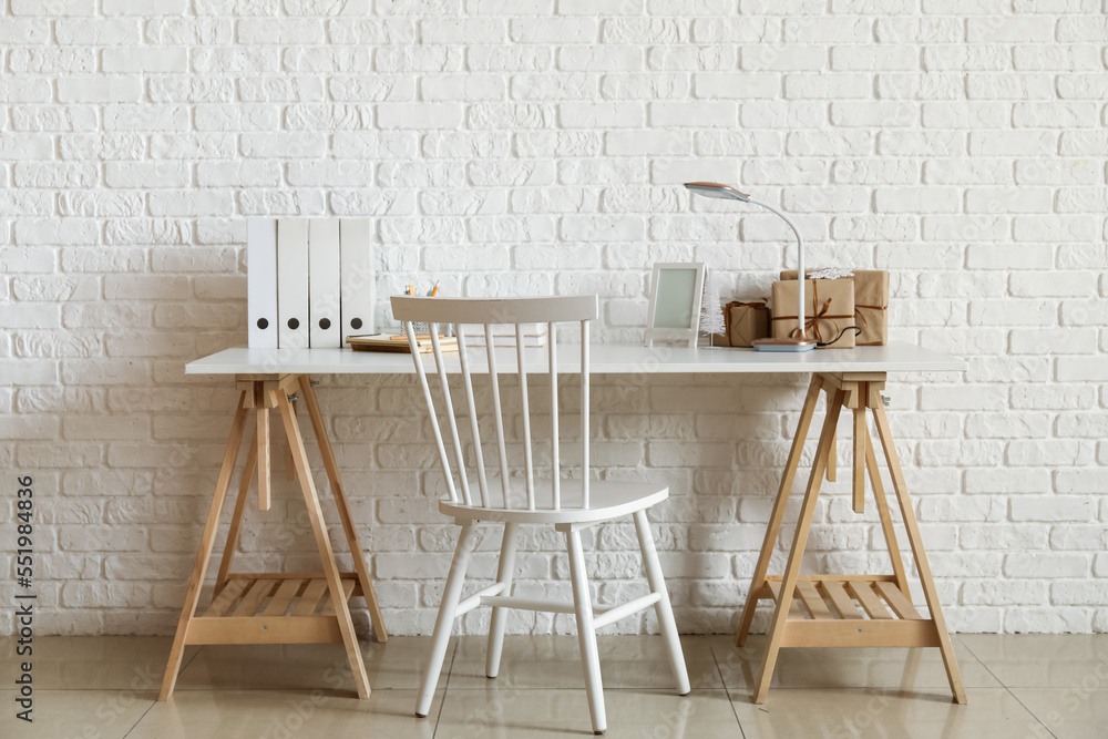 Workplace with frame, books, lamp and Christmas presents near white brick wall