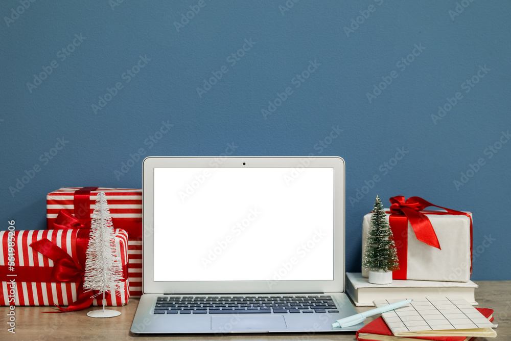 Laptop with Christmas presents on table near blue wall