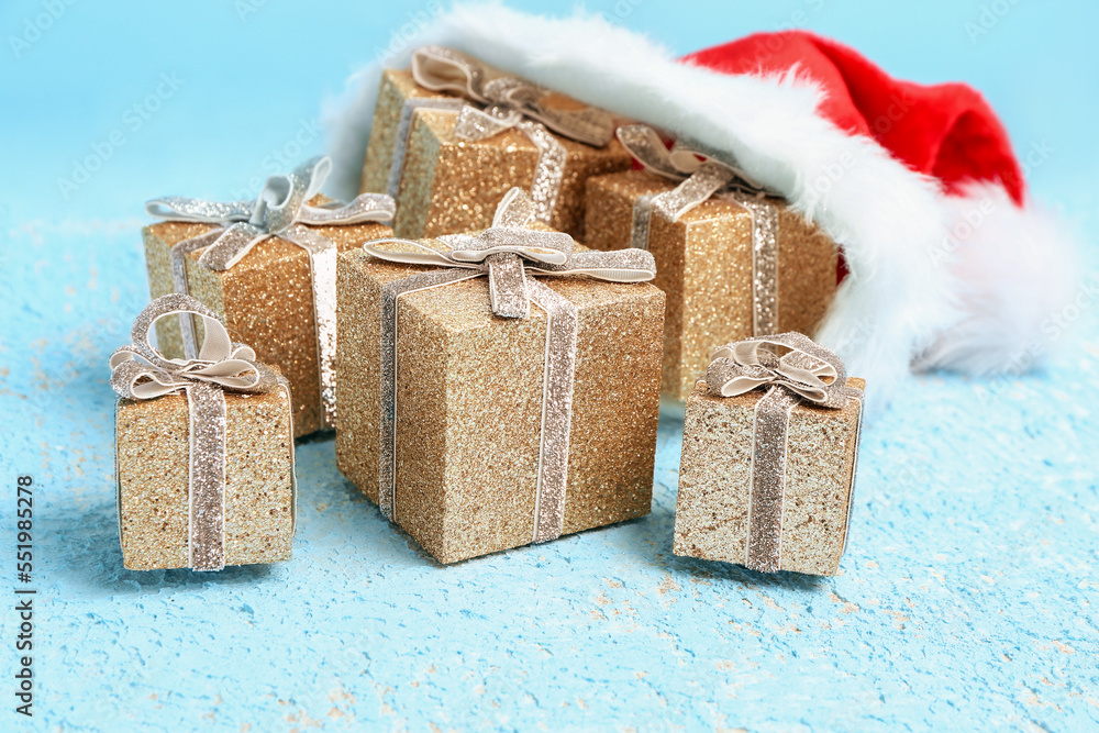 Santa hat with different Christmas gifts on color background