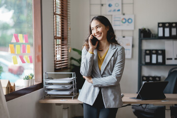 Asian businesswoman, real estate agent, talking on the phone with a customer about the details of selling a house How to buy a house step by step in the office and use the tablet.