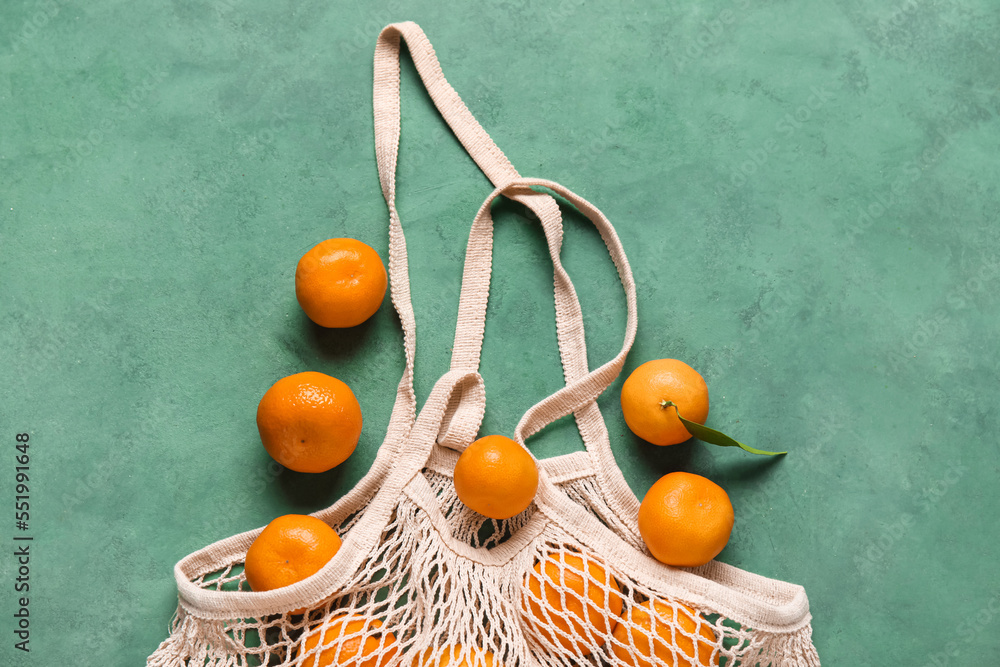 Shopping string bag with ripe tangerines on color background