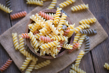 Wall Mural - Pasta raw macaroni on wooden bowl background, close up raw macaroni spiral pasta uncooked delicious whole grain fusilli pasta for cooking food