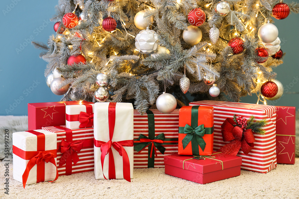 Gifts under glowing Christmas tree near blue wall