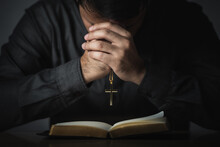 Crop Picture Of Religious Man Praying Holding Necklace Of Crosses And Bible Verses Praying Holy Blessings Sitting On The Table Gray Background. Spirituality And Religion. Christian Prayer Religion.