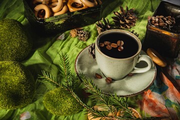 Wall Mural - Still life- a cup of hot coffee and roasted beans. Breakfast mug on a dark green background- table is decorated with sprigs of spruce.