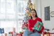 © StockPhotoRepublic - Cute beautiful young asian lady woman wearing reindeer headband holding a green color gift box with bells and posing in front a big Christmas tree with lots of decoration lights gift box and ornaments