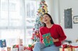 © StockPhotoRepublic - Cute beautiful young asian lady woman wearing reindeer headband holding a green color gift box with bells and posing in front a big Christmas tree with lots of decoration lights gift box and ornaments