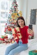 © StockPhotoRepublic - Cute beautiful young asian lady woman wearing reindeer headband selfie with her mobile phone holding gift box posing in front a big Christmas tree with lots of decoration lights gift box and ornaments