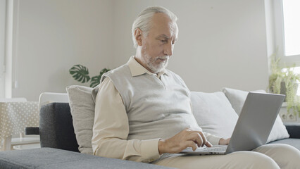 Concentrated senior man learning to use laptop at home, challenge of new technology