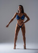 © VlaDee - Female bodybuilder in blue bikini standing in studio. Fit woman on high heels