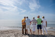 gruppo di 5 anziani in spiaggia in piedi  guardano abbracciati  l'orizzonte in lontananza 